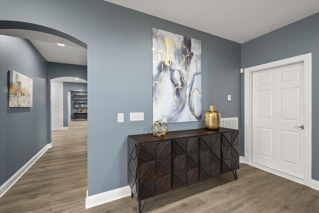 hall featuring arched walkways, wood finished floors, and baseboards