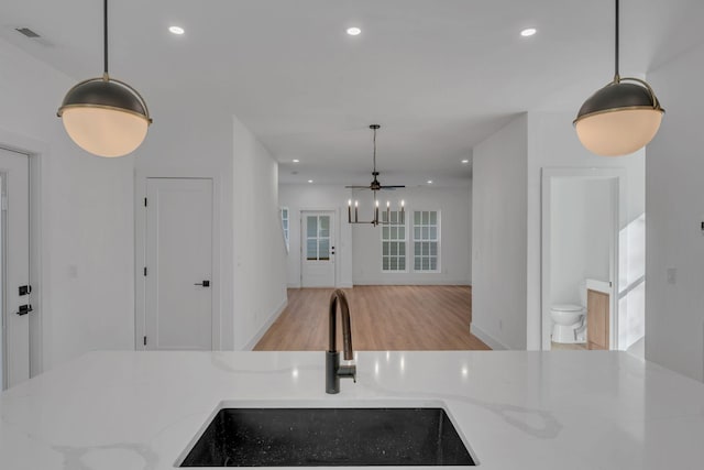 kitchen with light stone counters, light wood-type flooring, a sink, and recessed lighting