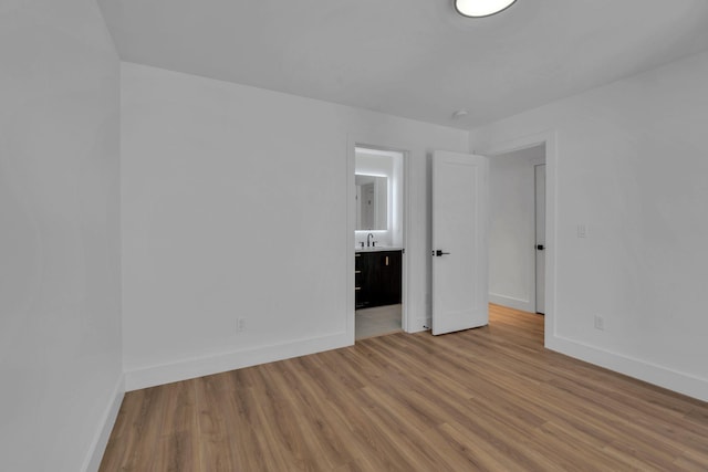 unfurnished bedroom featuring ensuite bathroom, wood finished floors, and baseboards