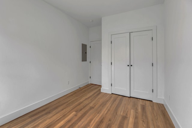 unfurnished bedroom with a closet, wood finished floors, electric panel, and baseboards