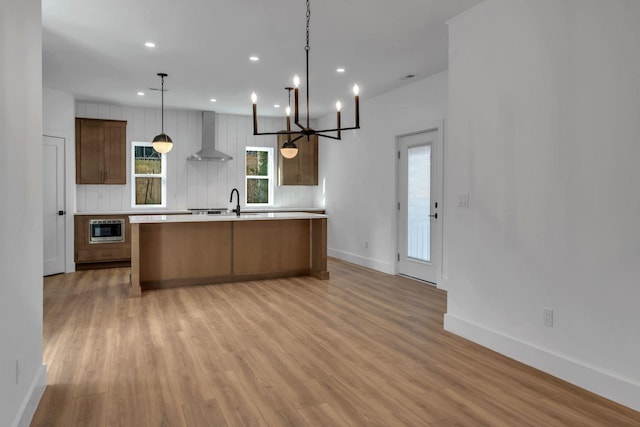 kitchen featuring a center island with sink, recessed lighting, light countertops, light wood-style flooring, and wall chimney exhaust hood