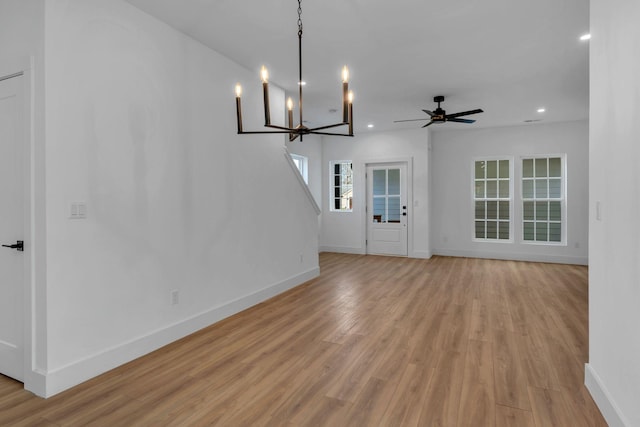 unfurnished living room featuring ceiling fan with notable chandelier, recessed lighting, light wood-style flooring, and baseboards