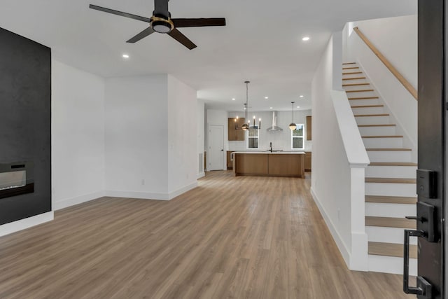 unfurnished living room with heating unit, stairs, ceiling fan with notable chandelier, light wood-style floors, and recessed lighting