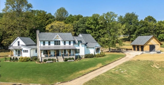 rear view of property featuring a chimney, covered porch, a lawn, driveway, and an outdoor structure