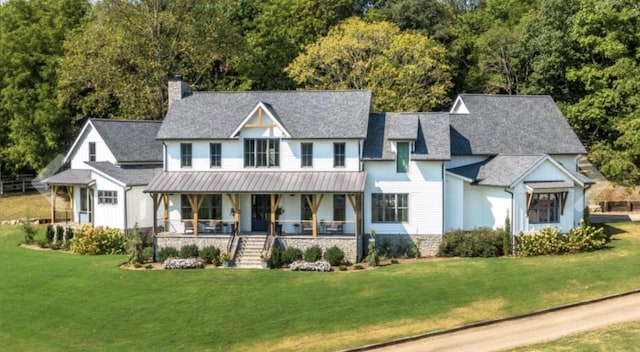 view of front of house with a chimney, covered porch, a standing seam roof, metal roof, and a front lawn