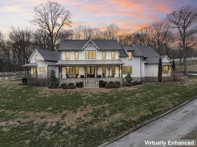 back of house at dusk featuring a porch, a standing seam roof, a yard, and a chimney