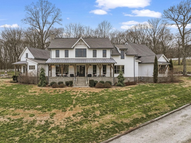 view of front of house with covered porch, a chimney, a front lawn, and a standing seam roof