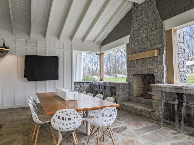 dining space with lofted ceiling with beams, a decorative wall, an outdoor stone fireplace, and stone tile floors