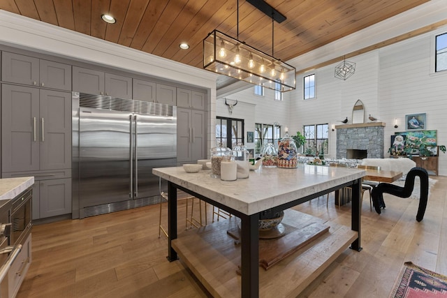 dining area with a stone fireplace, a high ceiling, wood ceiling, and light wood-style floors