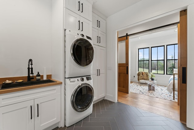 laundry area featuring a barn door, a sink, parquet floors, cabinet space, and stacked washer and clothes dryer