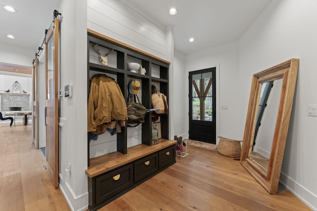 mudroom with a stone fireplace, a barn door, light wood-style flooring, recessed lighting, and baseboards