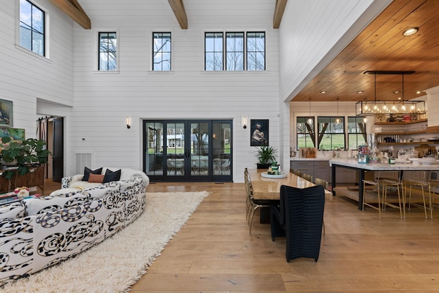 living room with beam ceiling, french doors, a high ceiling, light wood-style floors, and wood ceiling