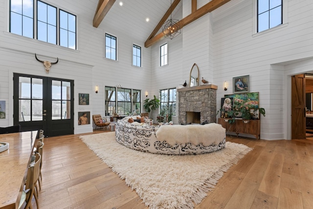 living room featuring beam ceiling, french doors, light wood finished floors, a stone fireplace, and high vaulted ceiling