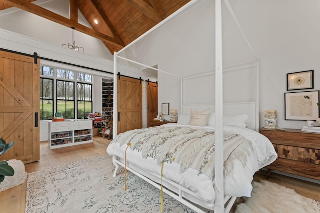 bedroom with a barn door, wooden ceiling, hardwood / wood-style floors, high vaulted ceiling, and beam ceiling