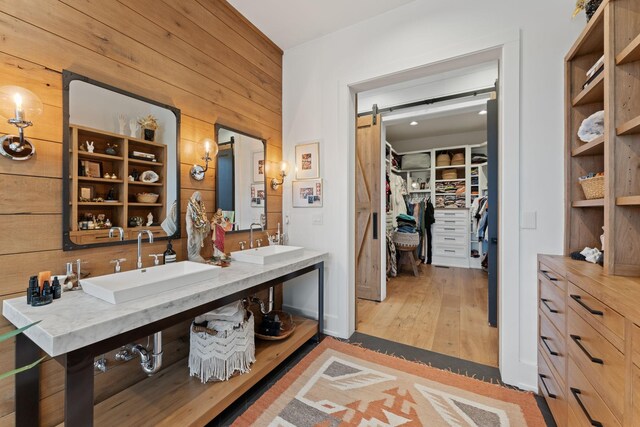 bathroom with a spacious closet, wood finished floors, a sink, and wooden walls