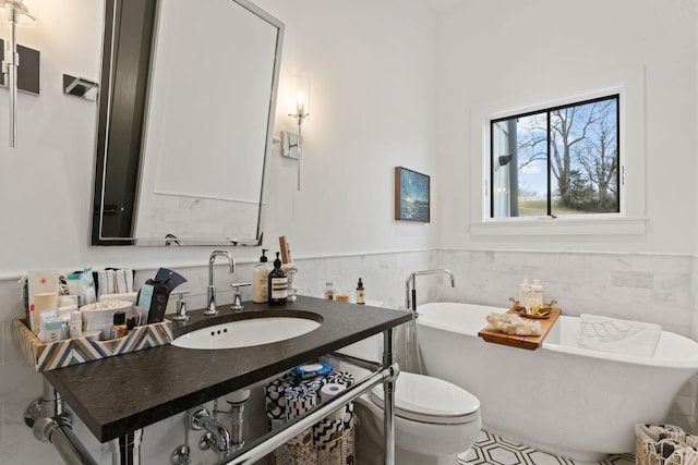 full bathroom featuring tile walls, a freestanding bath, toilet, wainscoting, and vanity