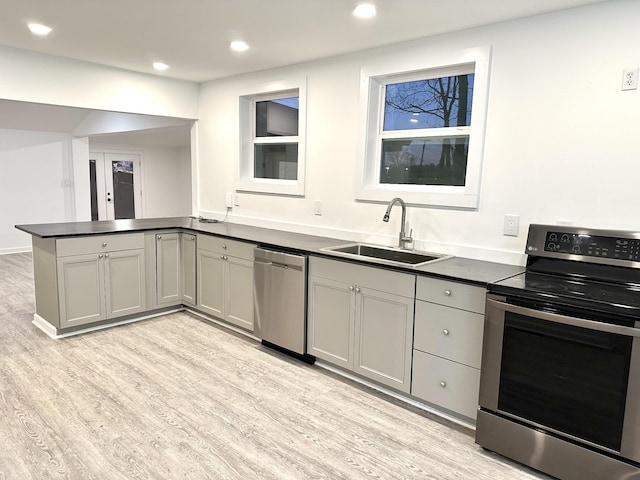 kitchen featuring stainless steel appliances, a peninsula, a sink, light wood-style floors, and dark countertops