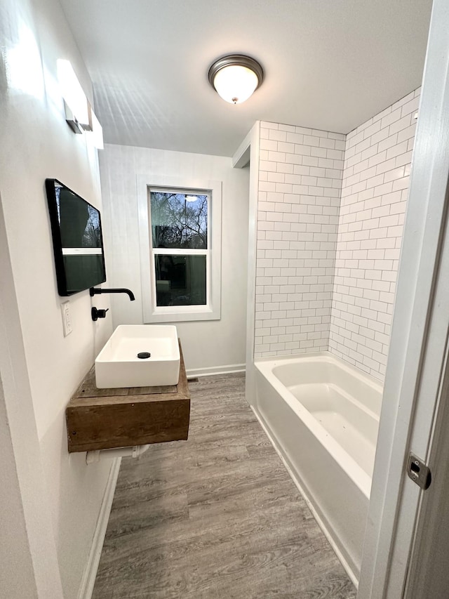 bathroom featuring baseboards, shower / bathing tub combination, a sink, and wood finished floors