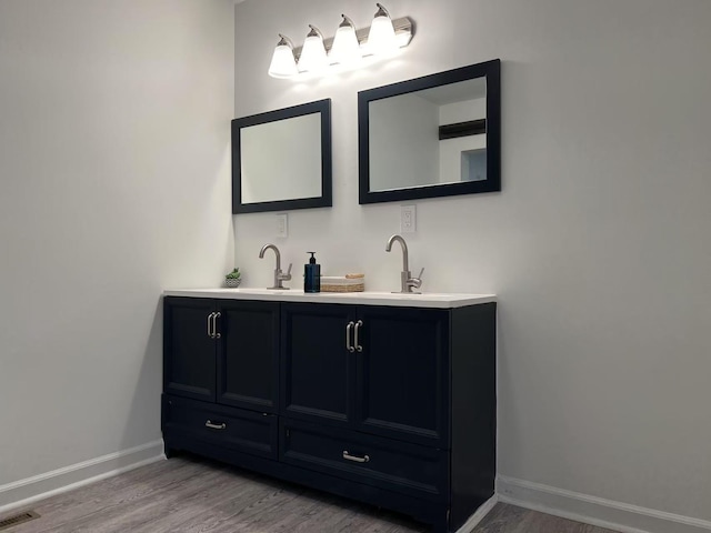 bathroom featuring double vanity, visible vents, a sink, wood finished floors, and baseboards