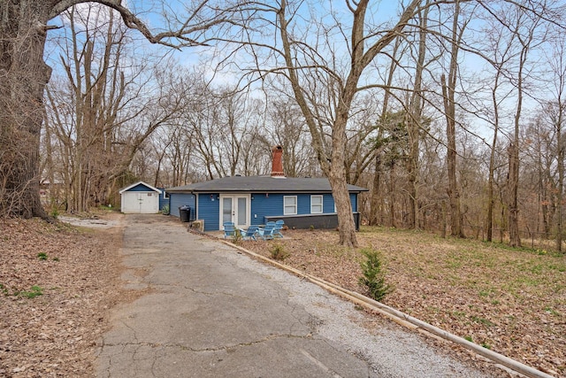 view of front of property featuring aphalt driveway, an outdoor structure, a chimney, and a detached garage