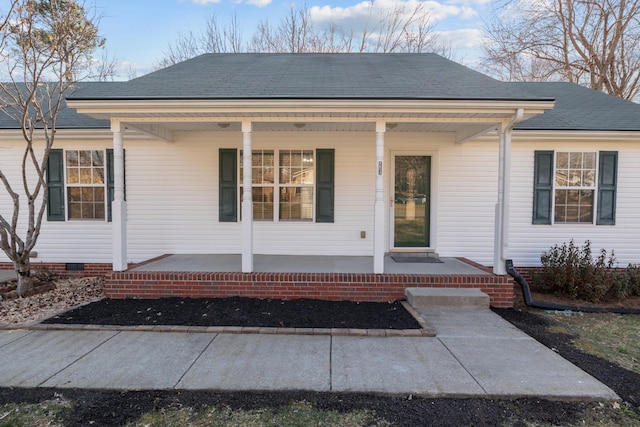 view of exterior entry with a shingled roof, crawl space, and covered porch