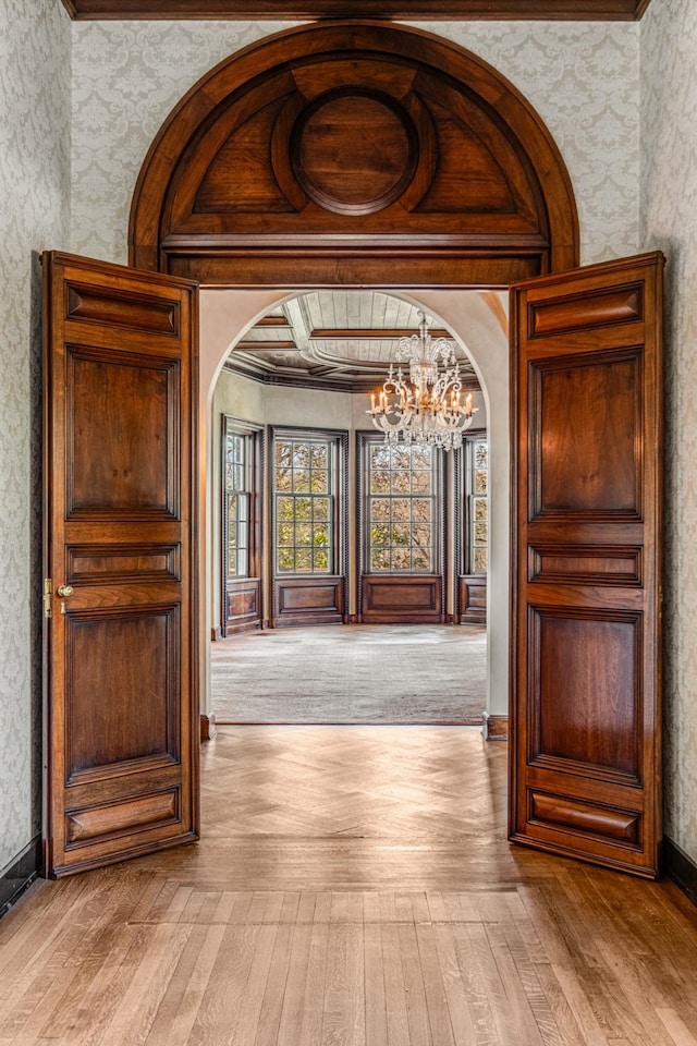 corridor with a chandelier, arched walkways, hardwood / wood-style flooring, and wallpapered walls