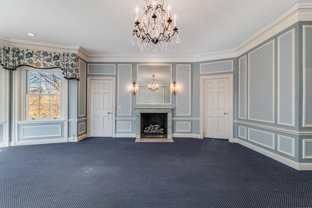 unfurnished living room with ornamental molding, dark colored carpet, a fireplace, a decorative wall, and a notable chandelier