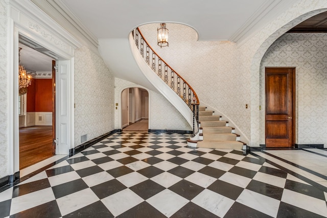 foyer featuring wallpapered walls, stairway, arched walkways, and a notable chandelier