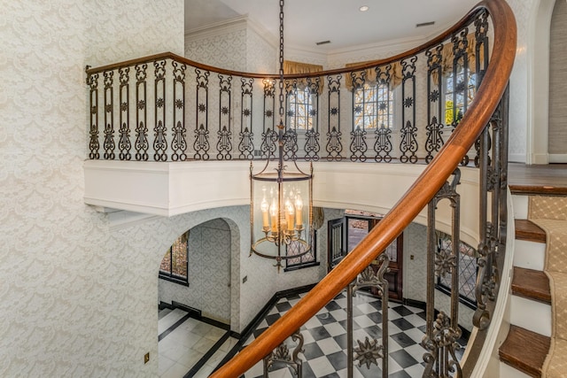 stairs with arched walkways, a chandelier, tile patterned floors, wallpapered walls, and crown molding