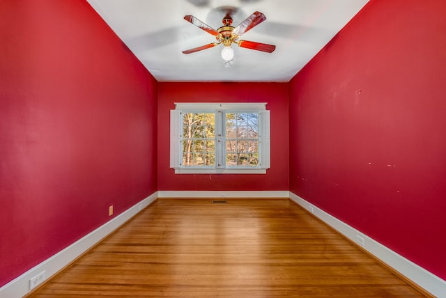 spare room with ceiling fan, visible vents, baseboards, and wood finished floors