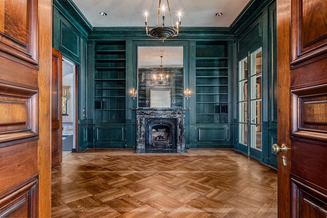 interior space featuring a chandelier, built in shelves, a decorative wall, a fireplace, and crown molding