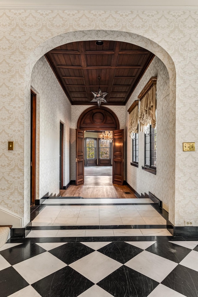 hall featuring arched walkways, baseboards, wooden ceiling, and wallpapered walls