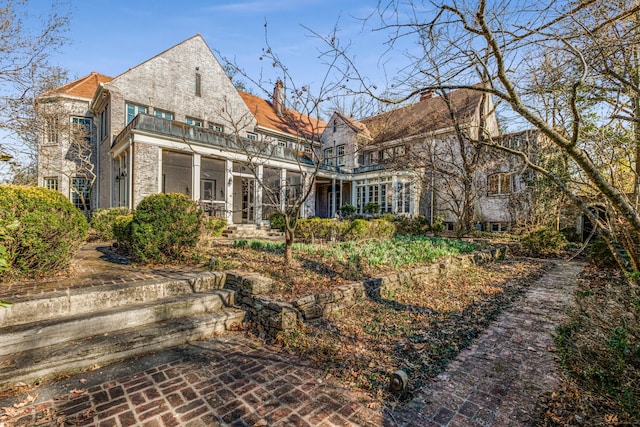 back of property featuring stone siding, a chimney, and a balcony