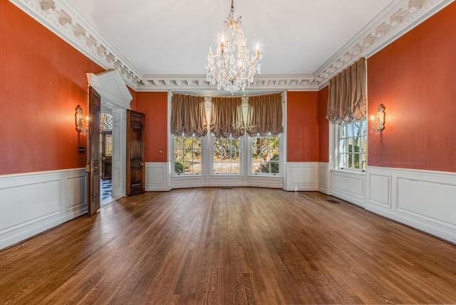 empty room featuring wainscoting, ornamental molding, a notable chandelier, and wood finished floors