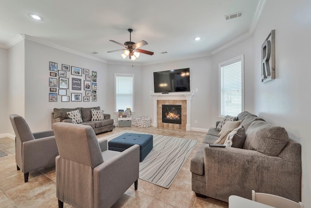 living area with crown molding, visible vents, a ceiling fan, a tile fireplace, and baseboards