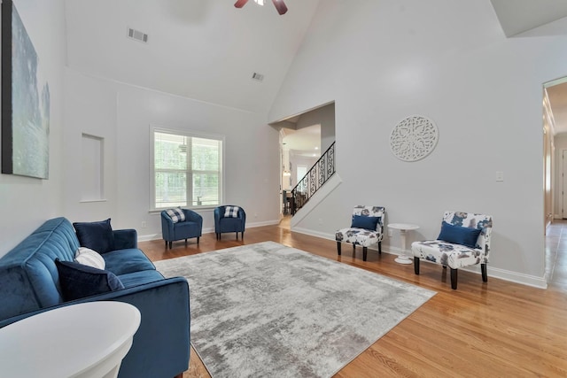 living area featuring stairway, light wood-style flooring, visible vents, and high vaulted ceiling