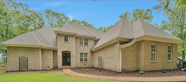 view of front of house featuring brick siding, a front yard, and roof with shingles