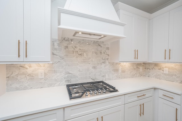 kitchen featuring custom range hood, light countertops, stainless steel gas stovetop, white cabinetry, and backsplash