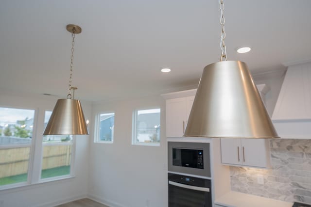 kitchen with pendant lighting, stainless steel microwave, white cabinets, and oven