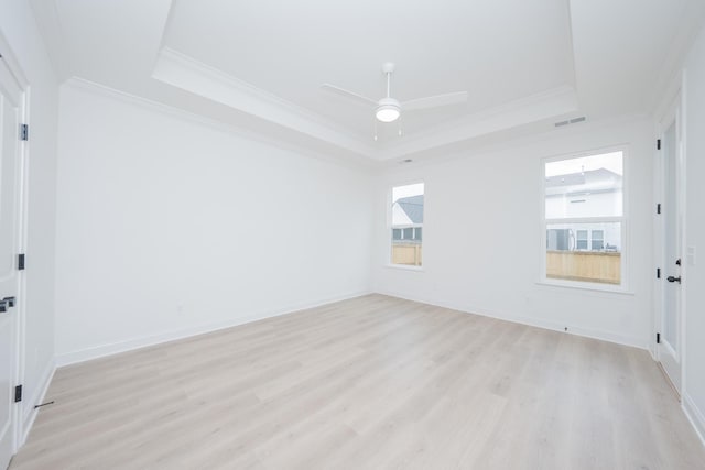 empty room with visible vents, a tray ceiling, light wood-style flooring, and crown molding