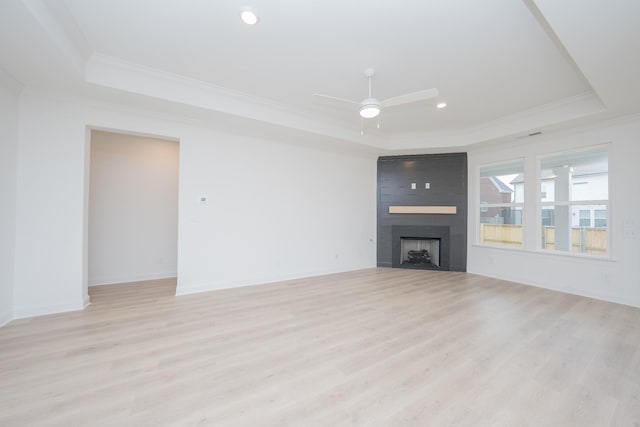 unfurnished living room featuring ornamental molding, a tray ceiling, light wood finished floors, and a fireplace