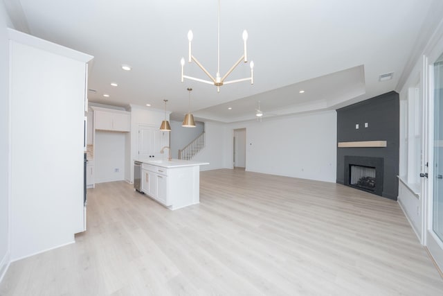 unfurnished living room featuring a tray ceiling, recessed lighting, light wood-style flooring, a large fireplace, and stairs