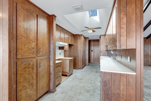 kitchen with under cabinet range hood, a skylight, brown cabinets, and a sink