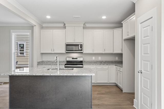 kitchen featuring an island with sink, appliances with stainless steel finishes, wood finished floors, crown molding, and a sink