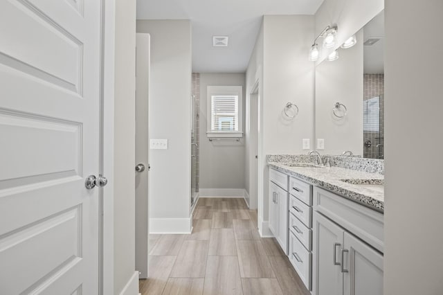 bathroom featuring double vanity, a stall shower, baseboards, visible vents, and a sink