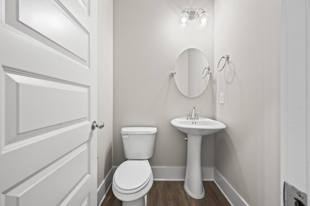 half bathroom with wood finished floors, toilet, and baseboards