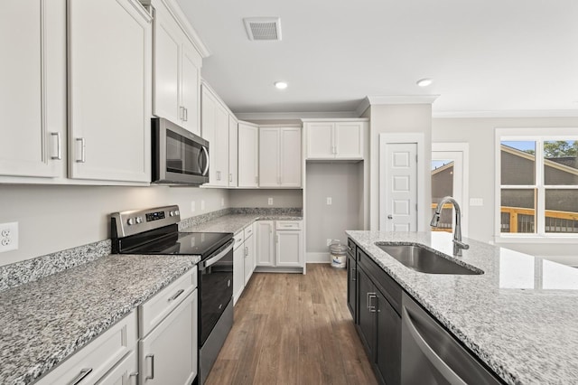 kitchen with stainless steel appliances, visible vents, white cabinetry, a sink, and wood finished floors