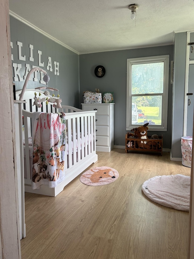 bedroom featuring a nursery area, a textured ceiling, ornamental molding, and wood finished floors