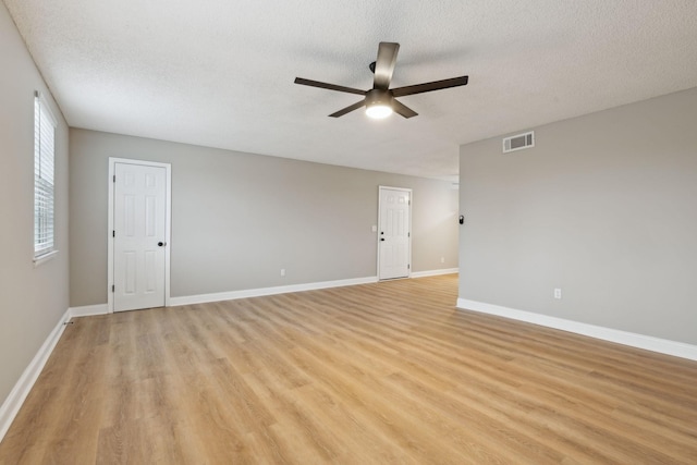 spare room with a textured ceiling, a ceiling fan, baseboards, visible vents, and light wood-style floors