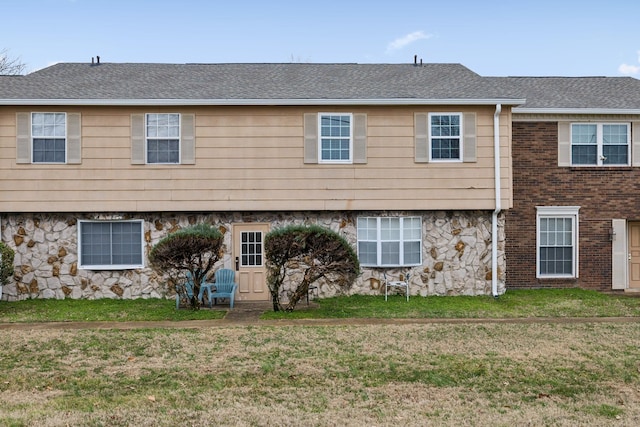 view of front of property with stone siding, a front lawn, and roof with shingles